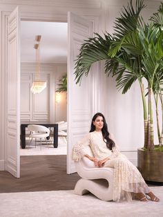 a woman sitting on a chair in front of a palm tree and potted plant