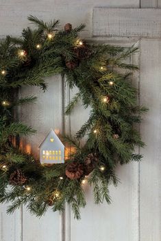 a christmas wreath hanging on the front door with lit lights and a house shaped ornament