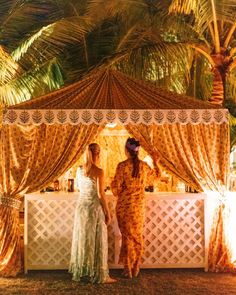 two women standing under a canopy in front of palm trees