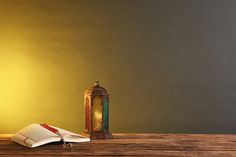 an open book sitting on top of a wooden table next to a lamp and lantern