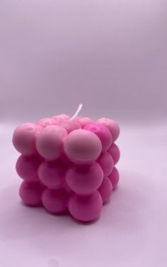 a candle that is made out of pink balls on a white surface with a single lit candle in the middle