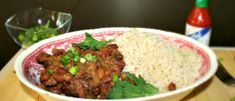 a bowl filled with rice and meat on top of a wooden table next to a bottle of ketchup