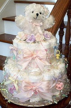 a white teddy bear sitting on top of a tiered cake with pink bows and diapers