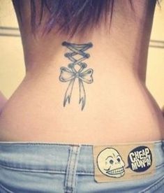 the back of a woman's neck with a bow and skull tattoo on it