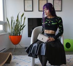 a woman with purple hair sitting on a chair in front of a window holding a purse