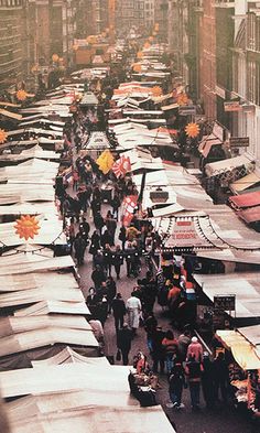 an outdoor market with lots of boats and people walking around it in the middle of the city