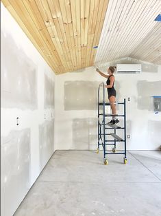 a woman on a scaffold painting the ceiling in a room with white walls