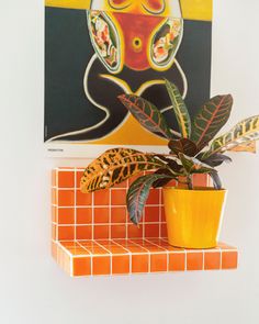 a potted plant sitting on top of a tiled shelf next to a painting hanging above it