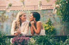 two beautiful women sitting next to each other in front of plants and hanging mason jars