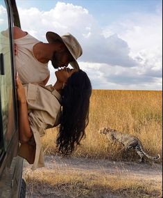 a man and woman leaning on the side of a vehicle in front of a cheetah