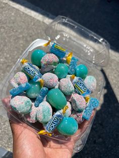 a person holding up a plastic container filled with blue and white candies on the street