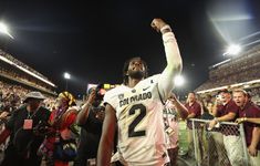 a football player is holding his fist up in the air as people watch from the sidelines