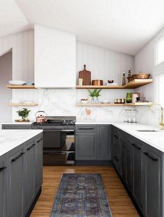 a kitchen with gray cabinets and white counter tops, wooden flooring and open shelving above the stove