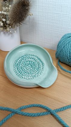 a blue plate sitting on top of a wooden table next to a ball of yarn