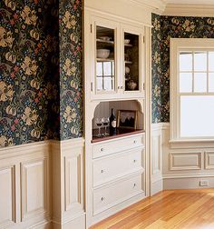 an empty room with wooden floors and floral wallpaper on the walls, along with white cabinets