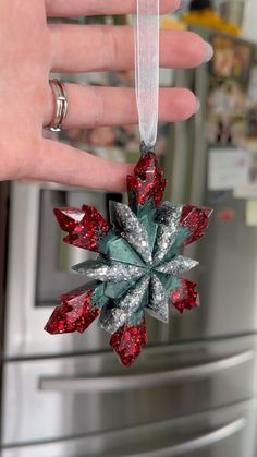 a hand is holding a christmas ornament in front of a silver refrigerator freezer