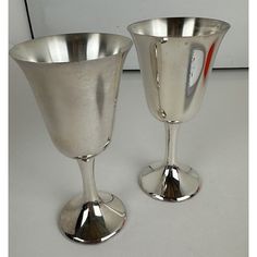 two silver goblets sitting side by side on a white counter top, one is empty