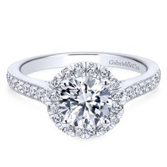 a white gold halo style engagement ring with round diamonds on the shoulders and sidestones