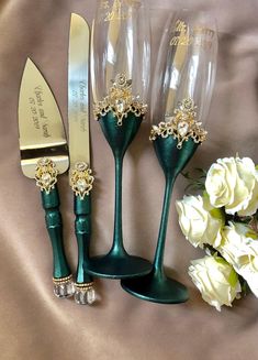 three wine glasses and a knife on a satin table cloth next to white flowers with gold trimmings