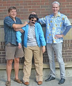 three men standing next to each other in front of a brick wall and wearing sunglasses