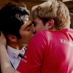 two young men kissing each other while wearing red shirts