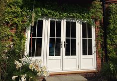 a white double door and window in front of a brick building with ivy growing on it