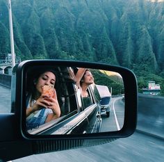 two women taking pictures in the rear view mirror of a car as it drives down a mountain road