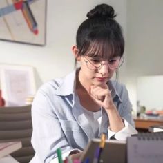 a woman sitting at a desk with her hand on her chin looking at the computer screen