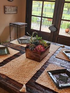 a wooden table topped with lots of plants on top of a brown rug next to a window