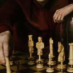 a man sitting at a chess board with his hand on the pawn's pieces