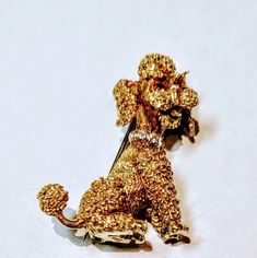 a gold colored brooch with a poodle on it's lapel, sitting on a white surface