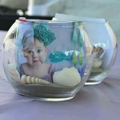 two glass bowls filled with sand and seashells on top of a purple table cloth