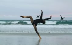 a man doing a handstand on the beach with two birds flying in the background