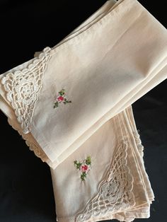 three white napkins with embroidered roses on them sitting next to each other in front of a black background