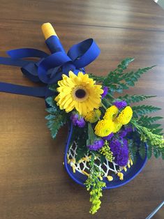 a blue vase filled with yellow and purple flowers on top of a wooden table next to a ribbon