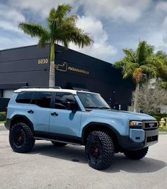 a light blue suv parked in front of a building with palm trees on the side