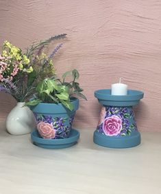 two blue flower pots with flowers in them sitting on a table next to a white vase