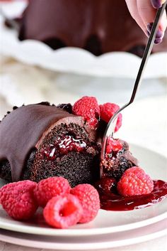 a chocolate cake with raspberries is being cut by a knife on a plate