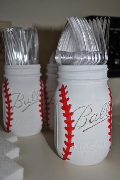 three white mason jars with silver lids and baseball stitching on the side, one has metal forks in it