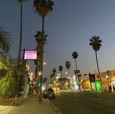 a car is parked on the side of the road at night time with palm trees in the background