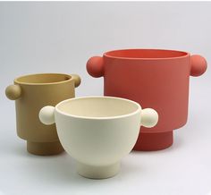 three different colored cups sitting next to each other on a white surface with one cup in the middle