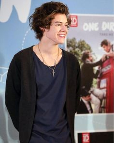 a young man is standing in front of a one direction sign and smiling at the camera