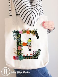 a woman holding a tote bag with the letter e painted on it and flowers