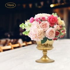 a gold vase filled with pink and red flowers on top of a white table cloth