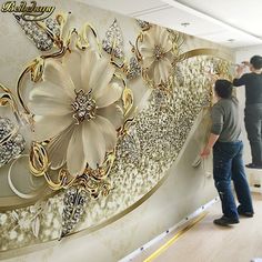 two men are painting a wall with gold and white flowers on it in an office