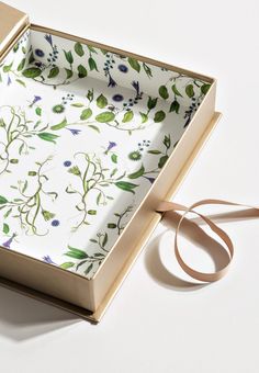 an open box with a ribbon on the side and flowers printed on it, sitting next to a pair of scissors