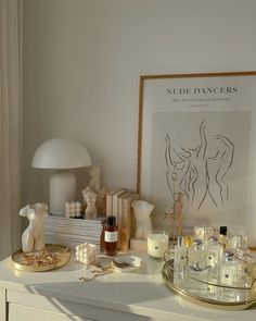 a white dresser topped with lots of bottles and candles next to a framed art piece