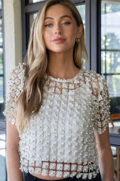 Add a playful touch to your wardrobe with the Laurel Crochet Lace Pearl Beaded Top. This cream-colored top features elegant crochet lace and stunning pearl beading, while the sheer fabric adds a touch of femininity. The back button neck detail and short sleeves complete this cropped top for a fun and flirty look. General Info: 100% Polyester Hand Wash Cold; Hang Dry Crochet Lace Pearl Beaded Sheer Outer Cami Lining Included Back Button Neck Detail Short Sleeves Cropped Fit Guide: Shape & Fit: Re Feminine Crochet Top For Spring Party, Spring Party Crochet Lace Top, Spring Party Lace Top With Crochet Lace, White Crochet Top For Spring Party, Spring Party Lace Top With Crochet Detail, Embellished Fitted Mesh Top For Spring, Elegant Pearl Embellished Tops For Spring, Chic Short Sleeve Lace Top For Wedding, Elegant Beaded Tops For Wedding