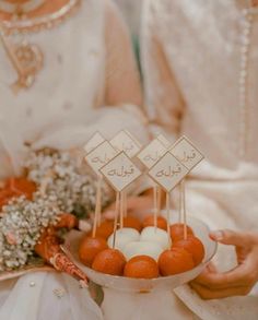 two people holding a plate with oranges on sticks and flowers in front of them