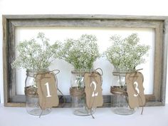 three mason jars with flowers in them on a shelf next to a wooden frame that says number one